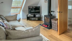 A modern living room with a sofa, a television, a fireplace, and a large window. - 2 bedroom accommodation in Clevedon (Clevedon)