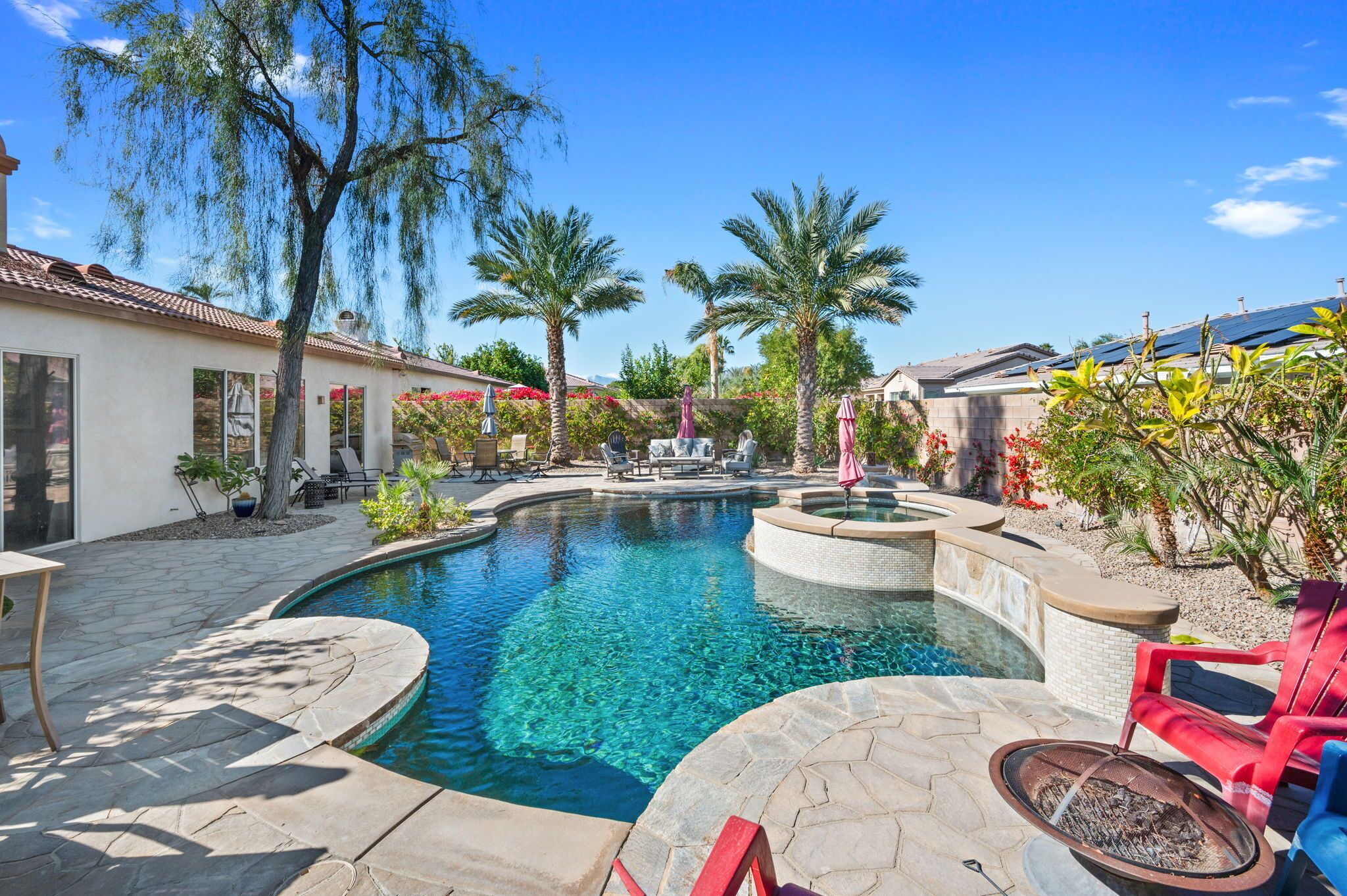 A swimming pool with a hot tub, surrounded by palm trees and outdoor seating.