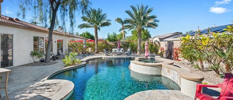 A swimming pool with a hot tub, surrounded by palm trees and outdoor seating.