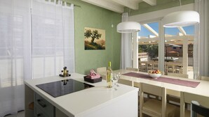 A modern kitchen with a central island, a dining area with a table and chairs, and a view of the outdoors through large windows. - Villa Olivia with Private Pool, Sauna, and Hot Tub – Just 800m from the Beach (Ližnjan)