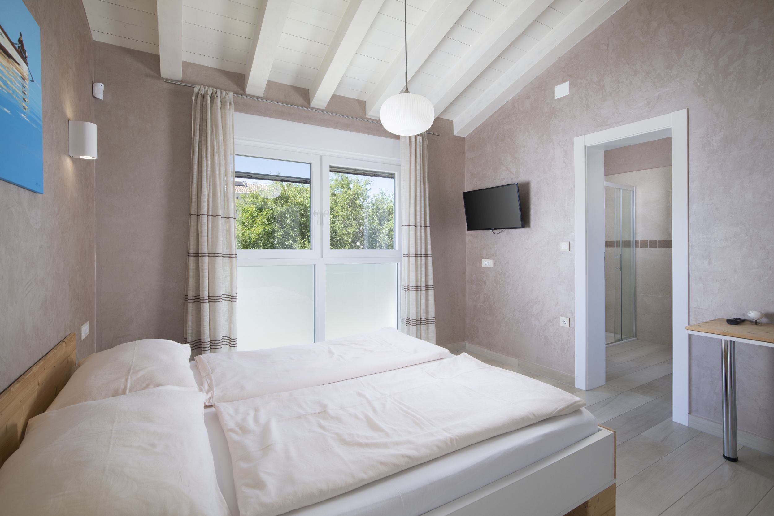 A bedroom with a bed, a TV mounted on the wall, and a window with curtains.