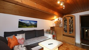 Una sala de estar acogedora con techo de madera, un sofá con cojines, una mesa de centro y un aparador con puertas de cristal.