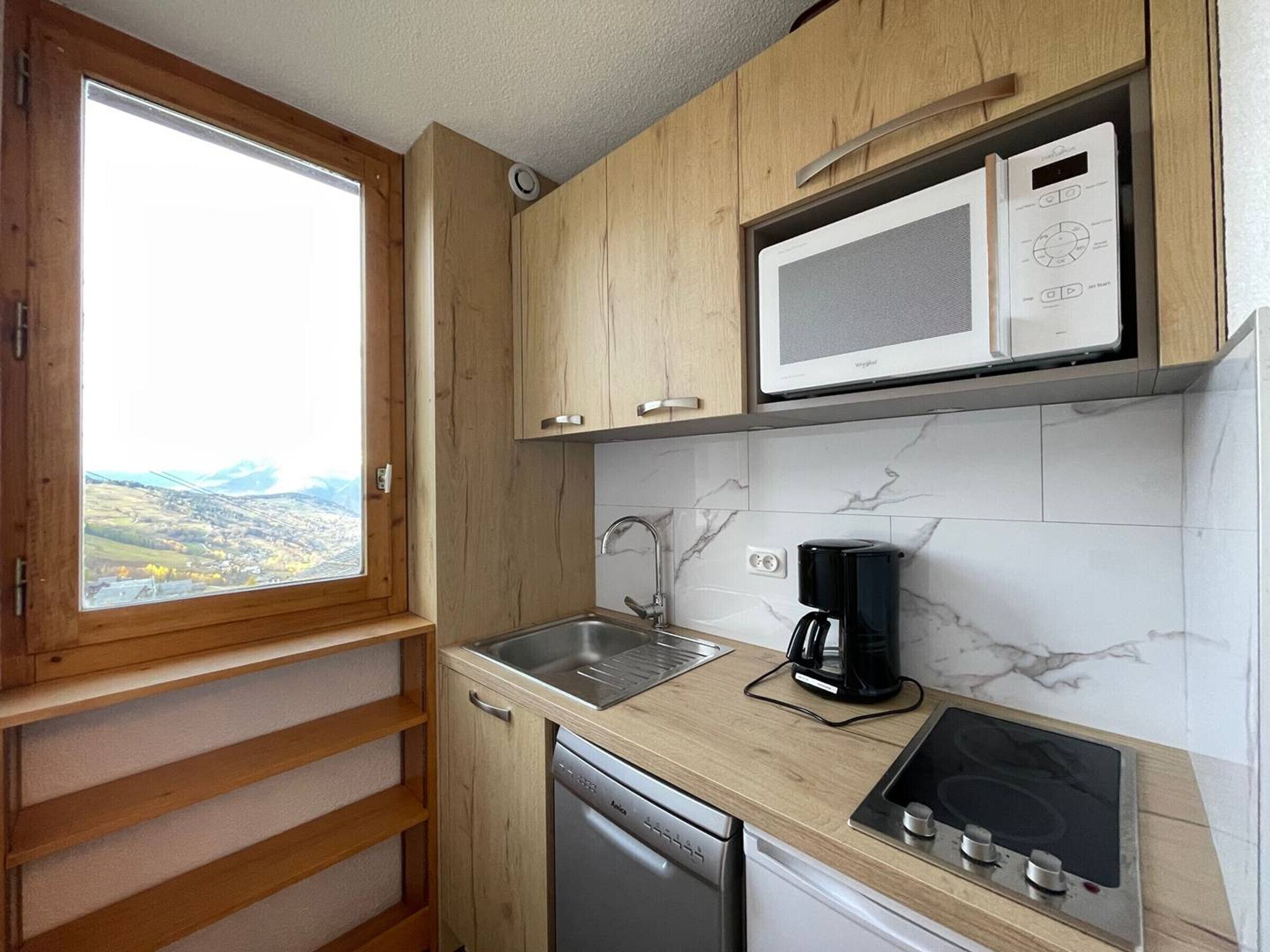A compact kitchen with wooden cabinets, a built-in microwave, a sink, a coffee maker, and a dishwasher.