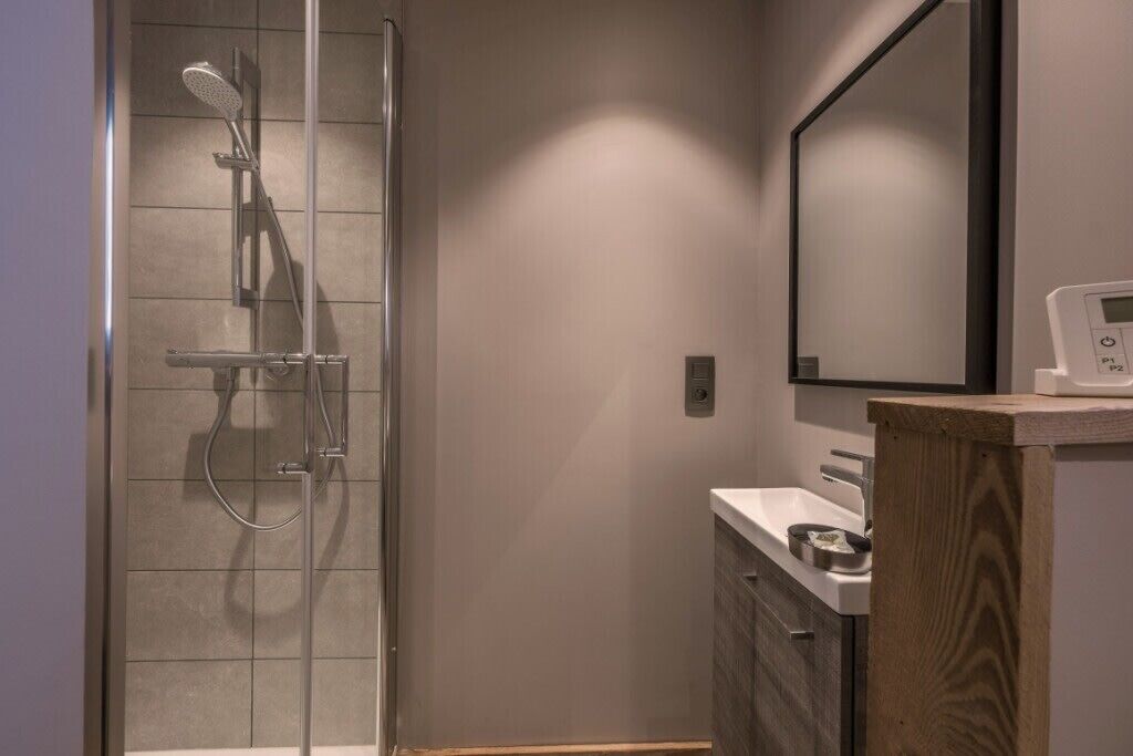Une salle de bain moderne avec une douche à parois de verre, un meuble-lavabo en bois et un miroir au-dessus du meuble.