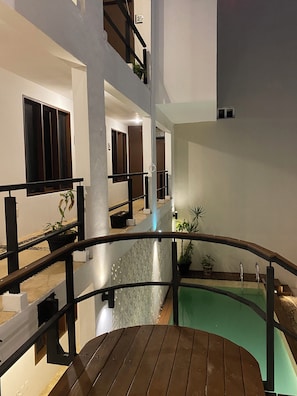 Un interior con varios niveles, una fuente central, barandillas de madera y plantas en macetas.