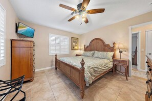 A bedroom with a wooden bed, a ceiling fan, a TV, a wardrobe, and a chair.
