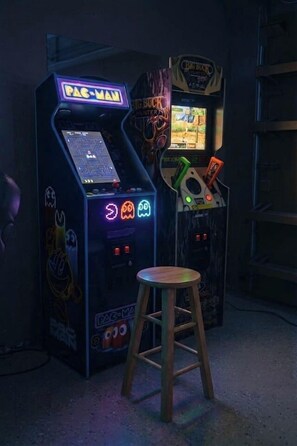 Arcade machines with neon signs, a stool, and a wall with a sign.