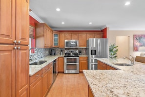 A modern kitchen with wooden cabinets, stainless steel appliances, granite countertops, and a tiled backsplash.