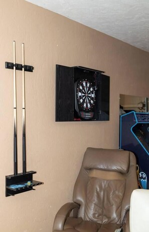 Eine an der Wand befestigte Dartscheibe, ein Dartscheibenständer und ein Ledersessel.