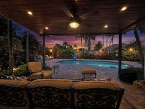 A covered outdoor area with a pool, lounge chairs, and a ceiling fan.