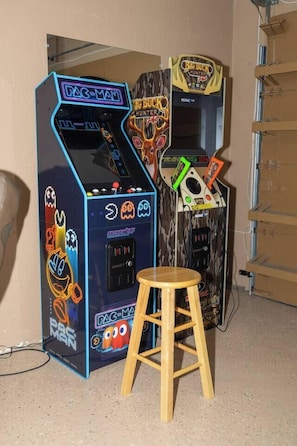 Kaksi peliautomaattia – Pac-Man-automaatti ja Big Buck Hunter -automaatti – ja niiden edessä puinen jakkara.