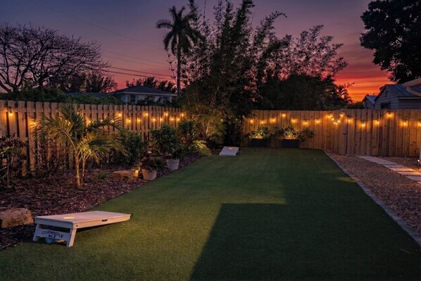 A backyard with artificial grass, a wooden fence, string lights, and potted plants.