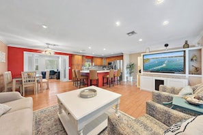A modern living room with a TV, seating, and a kitchen in the background.
