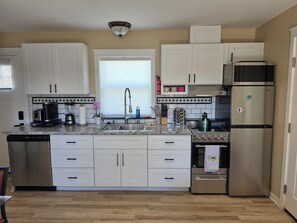 A modern kitchen with white cabinets, a stainless steel refrigerator, a built-in oven, and a dishwasher.