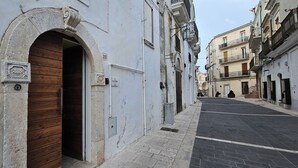Une rue étroite, avec une porte en bois et un arc en pierre, bordée d’immeubles dotés de balcons et d’enseignes.