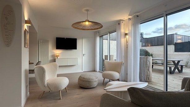 A modern living room with a flat-screen TV, comfortable seating, a large window, and a ceiling light fixture.