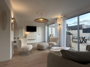Ein modernes Wohnzimmer mit Flachbildfernseher, bequemen Sitzgelegenheiten, einem großen Fenster und einer Deckenleuchte.