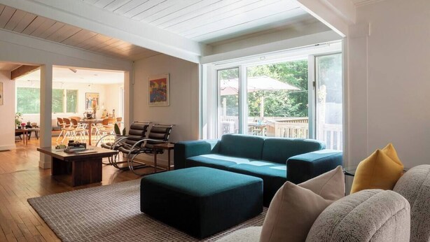 A spacious living room with a large window, a teal sofa, and a wooden ceiling. - ​Bright and Spacious Secluded Forest Home with Sprawling Yard and Private Brook (Cornwall)