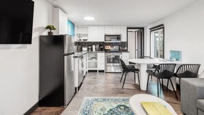 Une cuisine moderne avec des meubles blancs, des appareils en acier inoxydable et un coin repas comprenant une table ronde et des chaises noires.