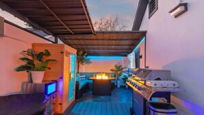 Une terrasse extérieure équipée d’un barbecue, d’un espace salon et d’un éclairage d’ambiance.