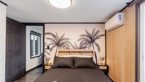 Une chambre d’hôtel comprenant un lit, deux oreillers, une table de chevet, un appareil de climatisation et un panneau mural en bois.