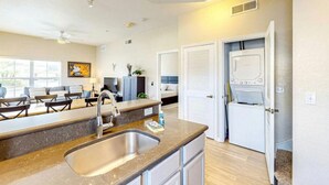 A modern kitchen with a sink, countertop, and built-in appliances. There is a seating area with chairs and a couch, and a window providing natural light. - 4 Bedroom 3 Bathroom Villas At Seven Dwarfs 12-108 (Kissimmee)