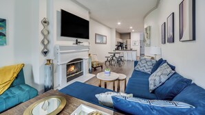 A modern living room with a fireplace, blue sofa, and a flat-screen TV mounted above it. - Lynn's Lodging (Austin)