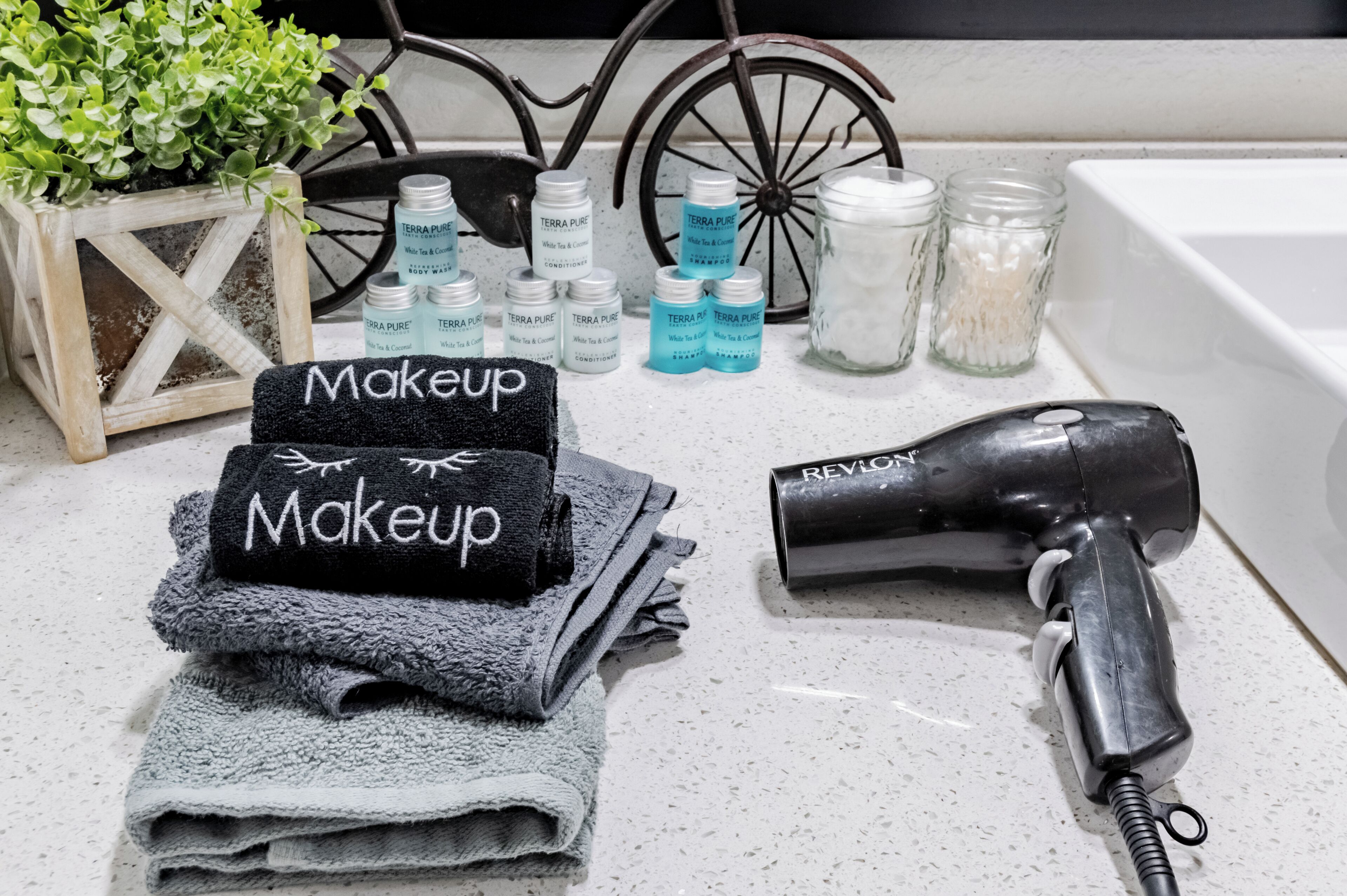 Un meuble-lavabo dans la salle de bain, avec une pile de serviettes, un sèche-cheveux et des flacons de gel douche et d’après-shampoing de la marque Terra Pure.
