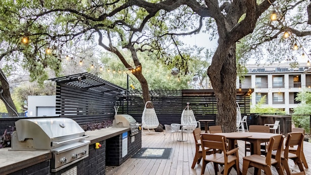 An outdoor patio with a grill, wooden tables, and chairs. - Lynn's Lodging (Austin)
