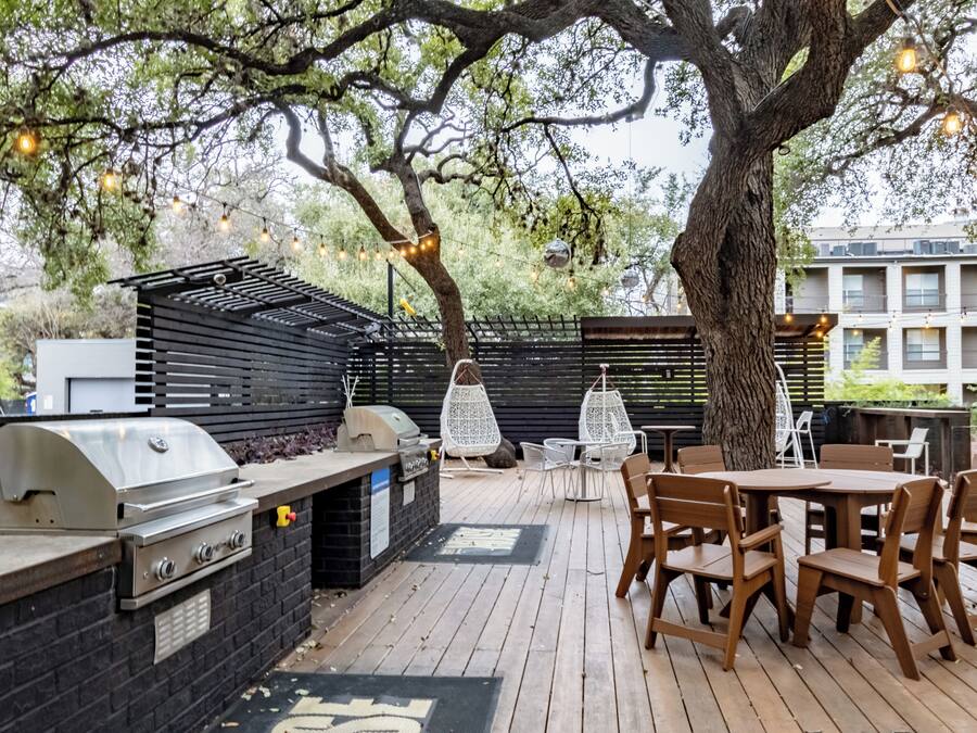 Een terras buiten met een barbecue, houten tafels en stoelen.
