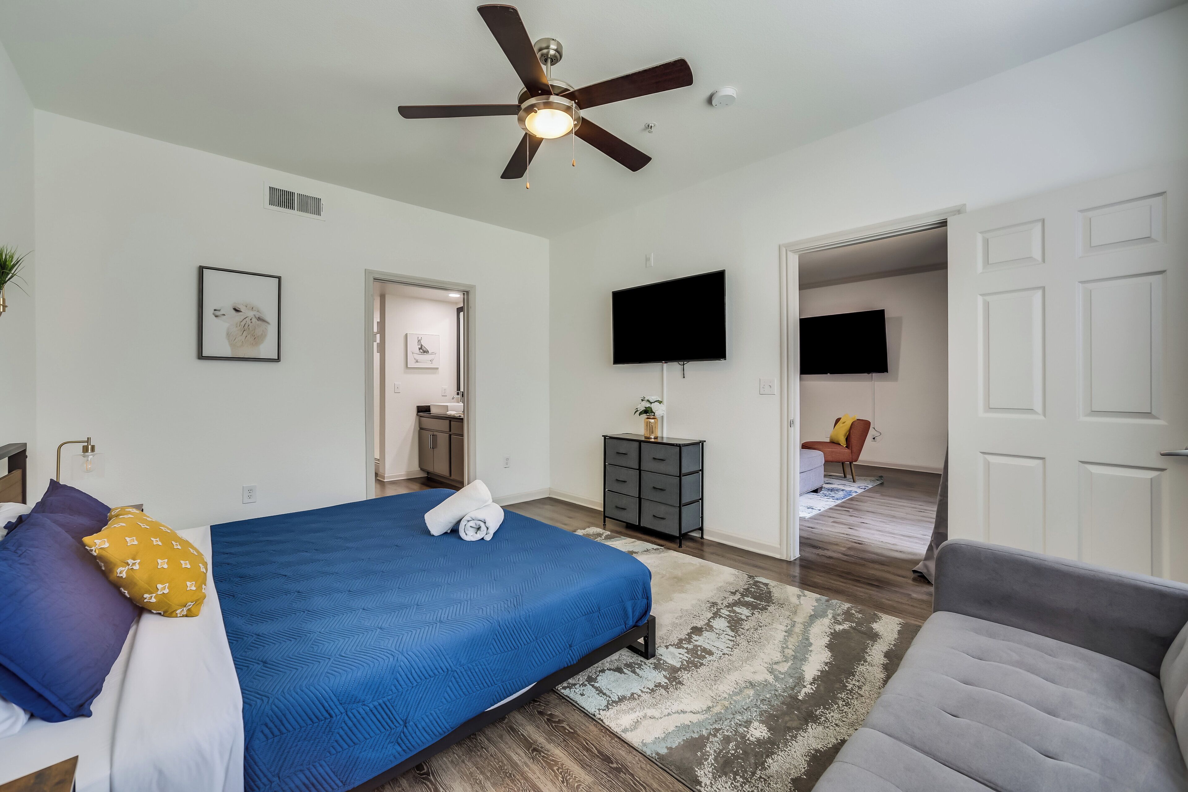 A bedroom with a bed, a ceiling fan, a TV, and a door leading to another room.