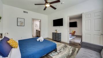 A bedroom with a bed, a ceiling fan, a TV, and a door leading to another room.