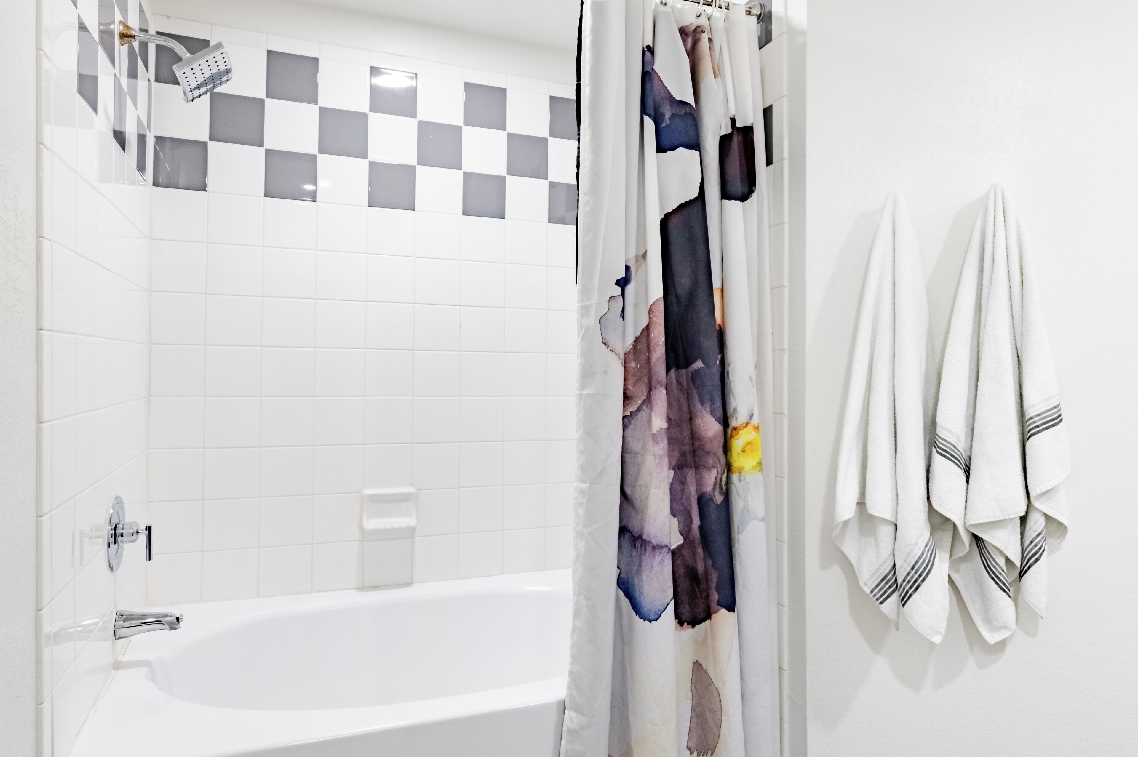 A bathroom with a white bathtub, a showerhead, and a checkered wall.