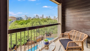 A balcony with wicker furniture and a view of a city skyline and greenery. - Lynn's Lodging (Austin)