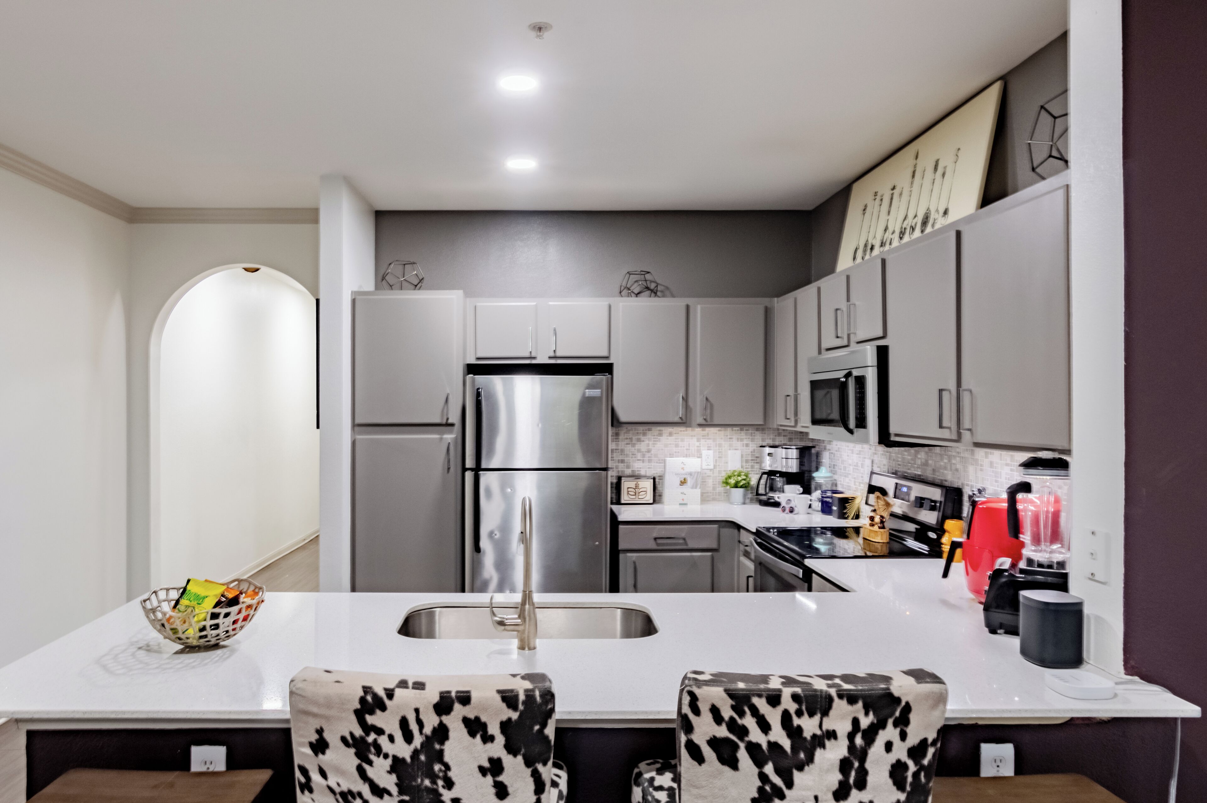 Una cocina moderna con una isla central, electrodomésticos de acero inoxidable y encimera blanca.