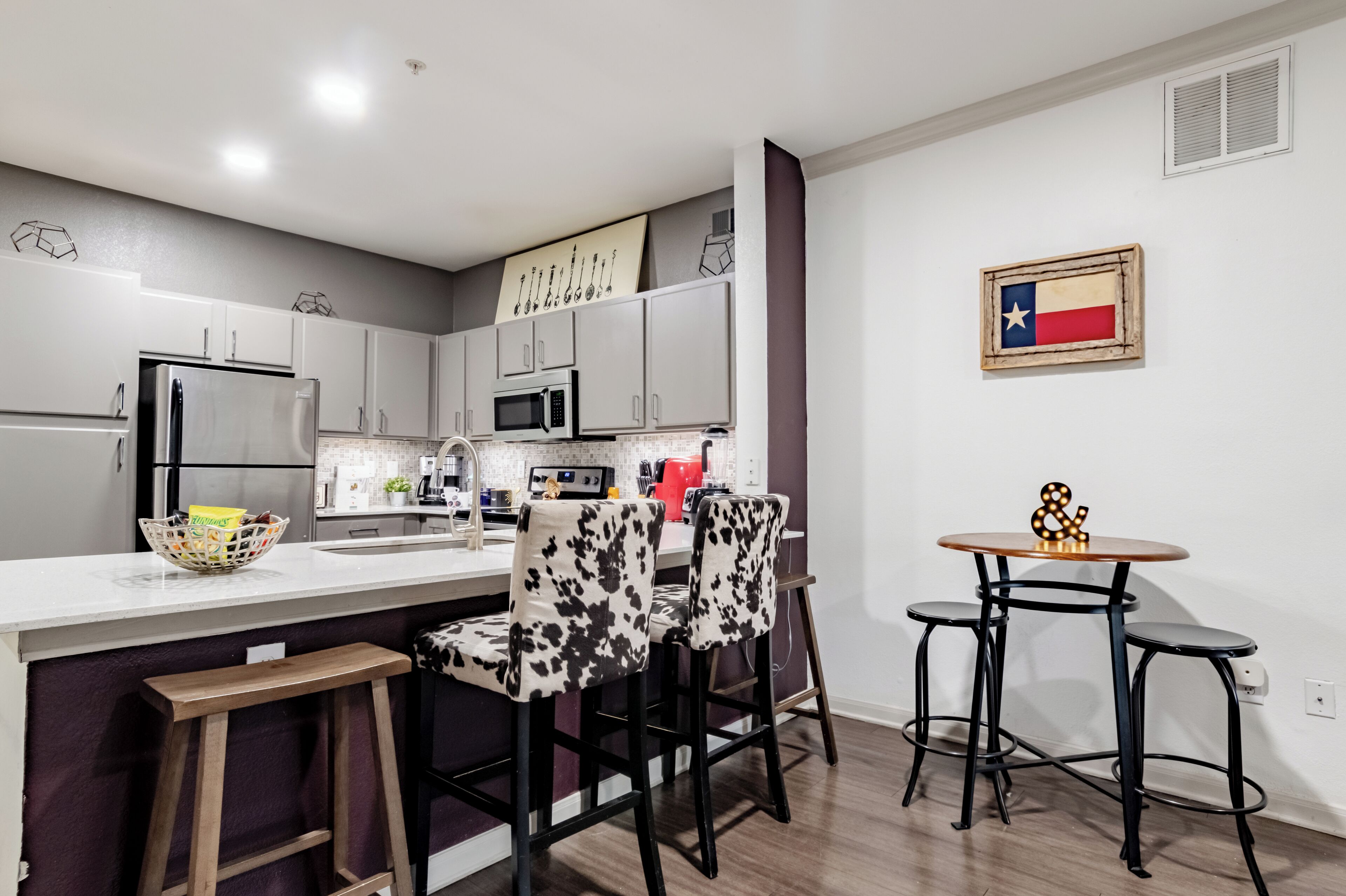 A modern kitchen with a central island, bar stools, a small table, and a Texas flag decoration.