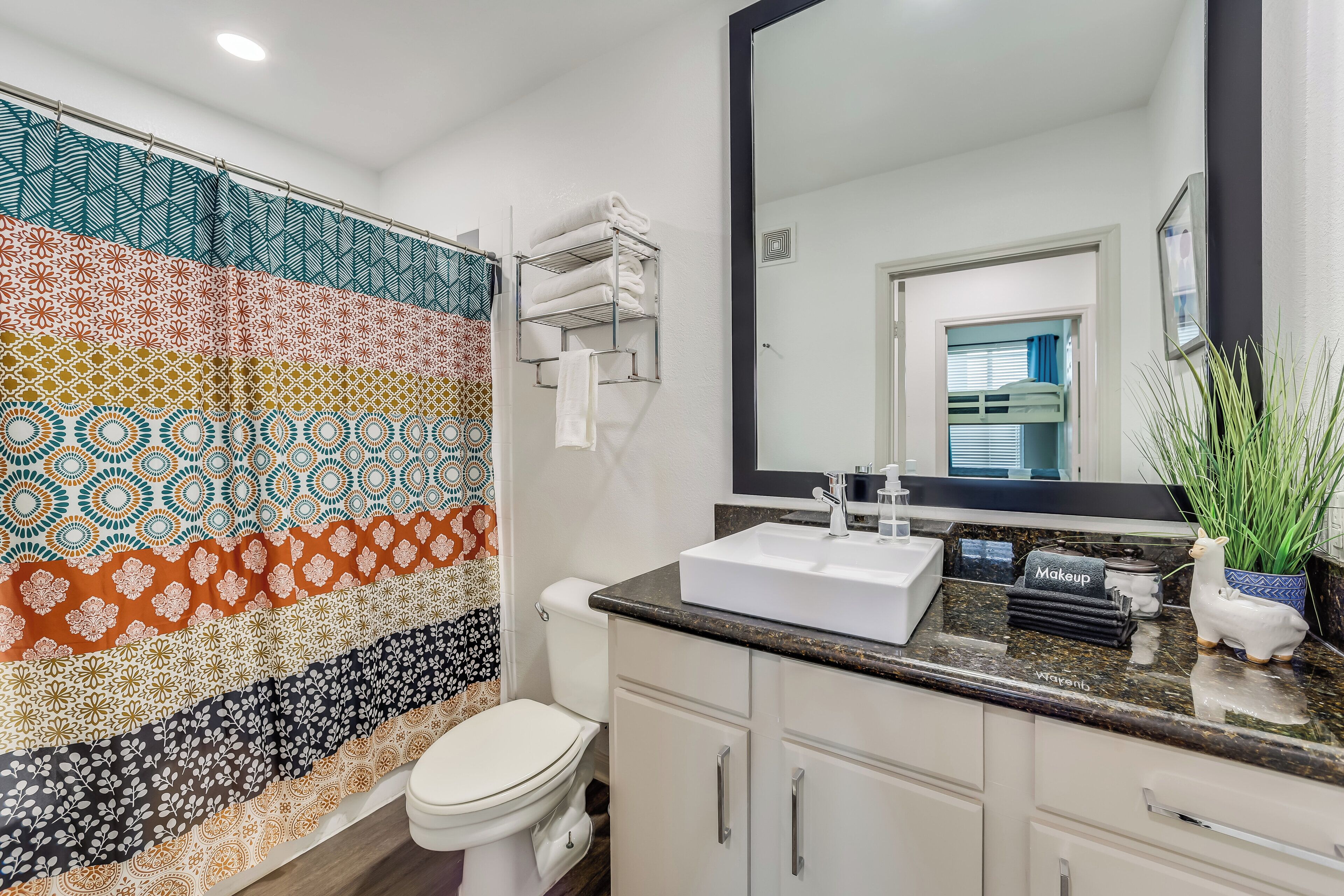 A bathroom with a patterned shower curtain, a white toilet, a sink with a mirror, and a cabinet.