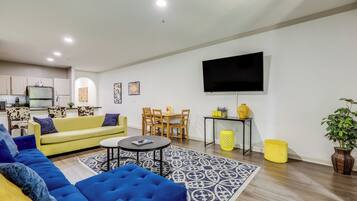 A modern living room with a yellow sofa, blue sofa, and a TV mounted on the wall.