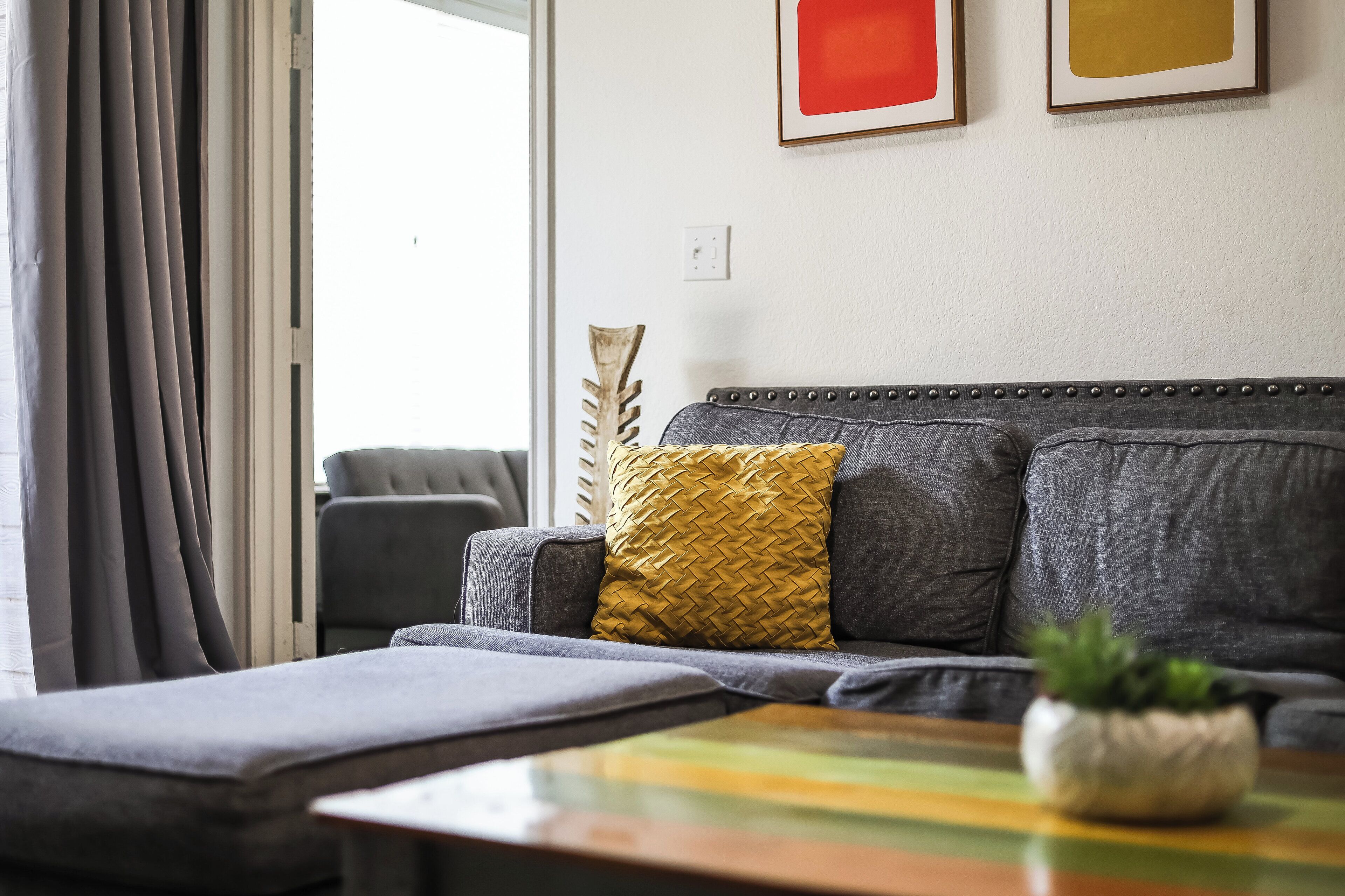 A modern living room with a grey sofa, a yellow woven pillow, and a small plant on a wooden coffee table.