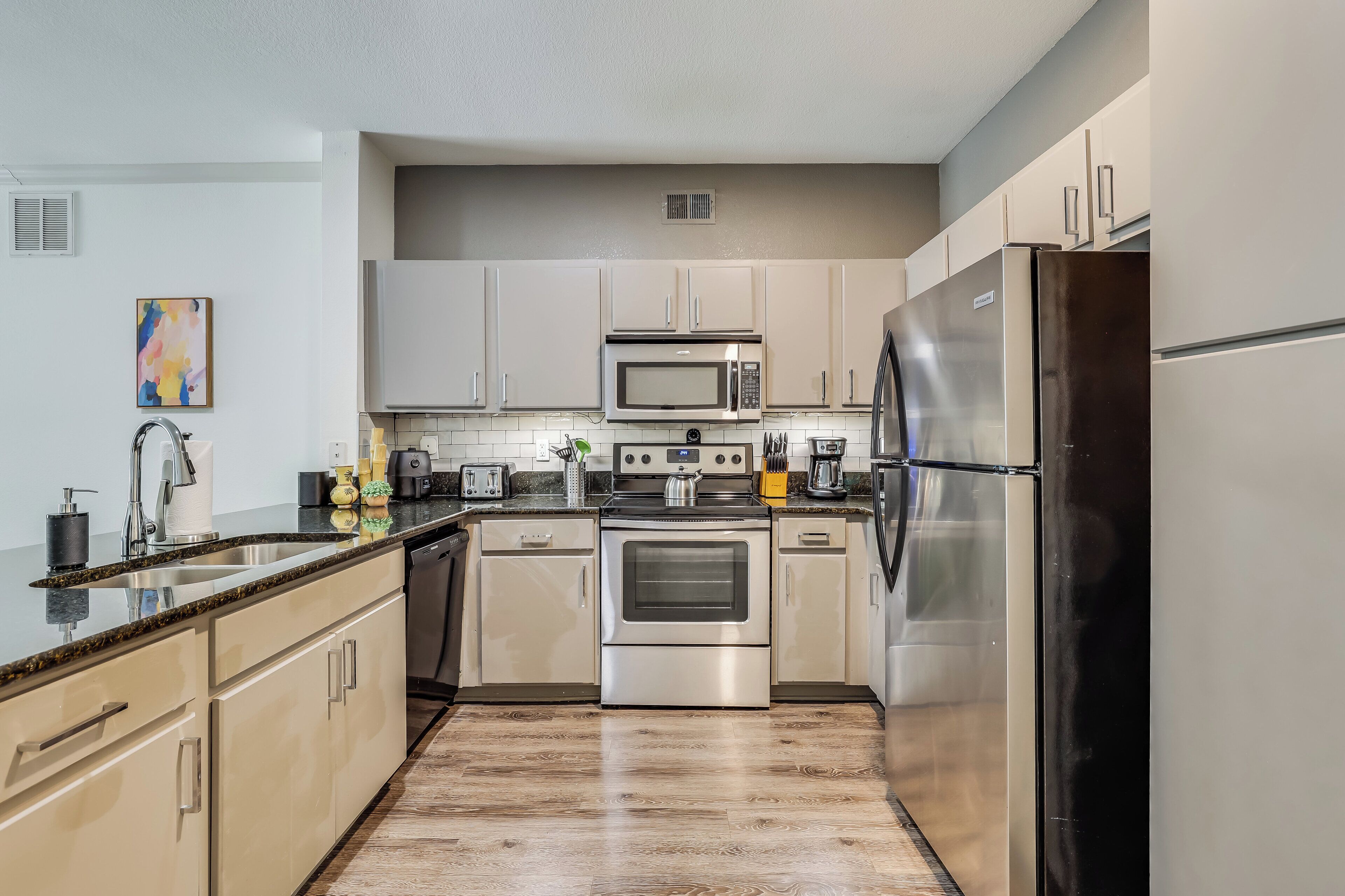 A modern kitchen with stainless steel appliances, light-colored cabinetry, and a granite countertop.