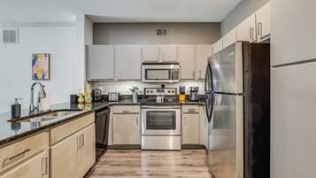 A modern kitchen with stainless steel appliances, light-colored cabinetry, and a granite countertop.