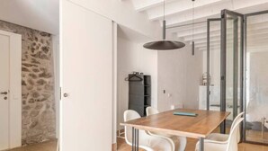 A modern dining area with a wooden table and white chairs, a hanging pendant light, and a glass partition. - Romantic apartment in idyllic nature setting (Barcelona)