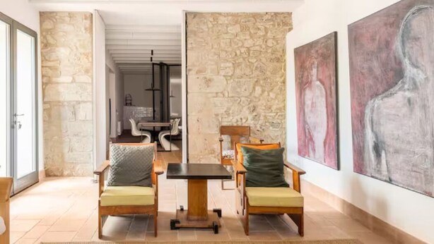 A spacious living area with a stone wall, a wooden table, and two chairs. - Romantic apartment in idyllic nature setting (Barcelona)