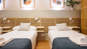 Et hotelværelse med to senge, træpaneler ved sengegavl, natborde og en potteplante.