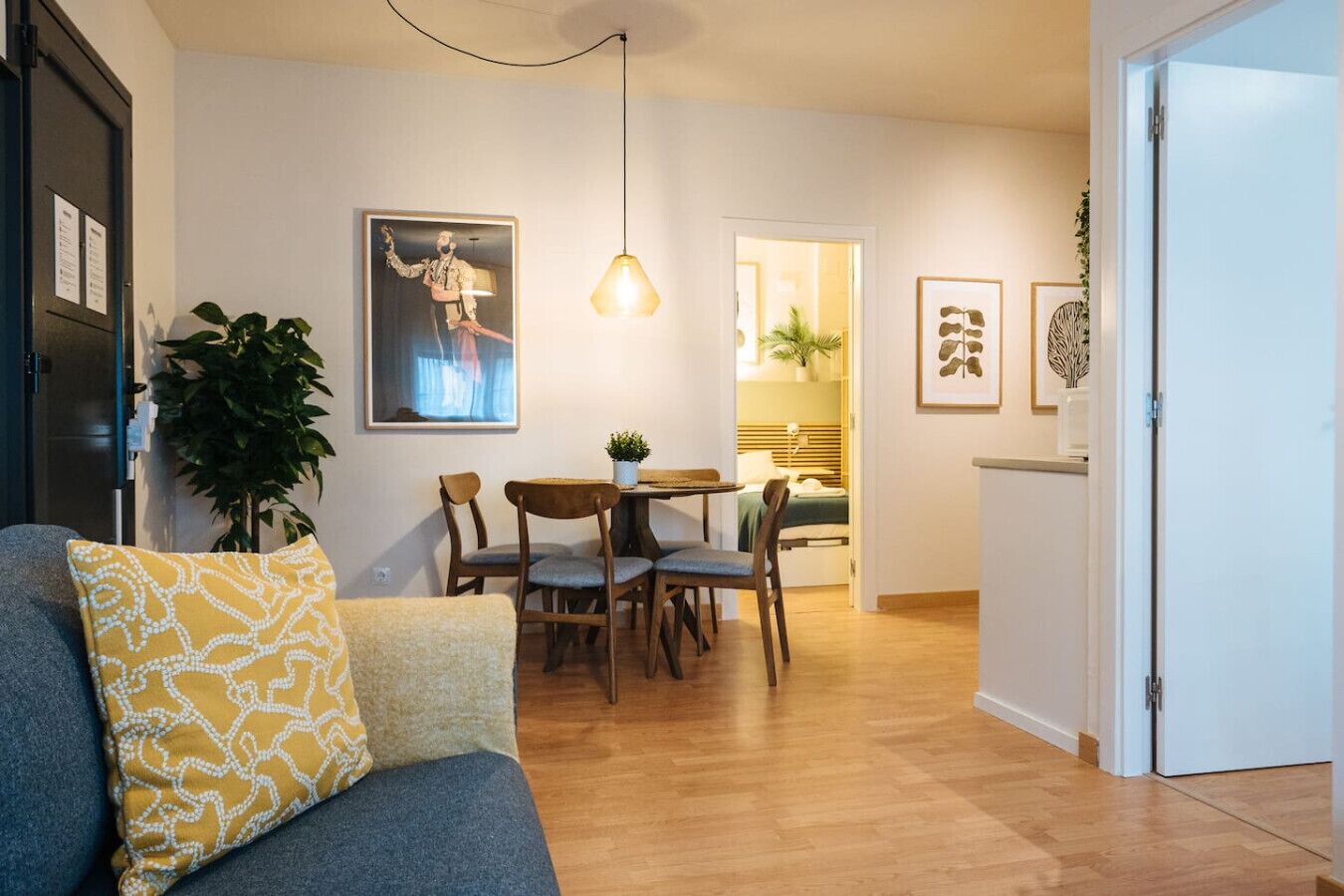 Uma sala de estar aconchegante com um sofá, uma mesa de jantar com cadeiras, um lustre e uma porta que dá para outro espaço.