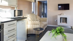 A compact living space with a kitchenette, a sofa, a small round table, and a television mounted on the wall. - 2 bedroom accommodation in Wilsthorpe (Wilsthorpe)