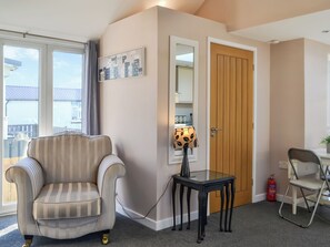 Een kamer met een gestreept fauteuil, een tafeltje met een lamp, een houten deur en een brandblusser.