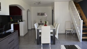 A modern kitchen with a dining area, a staircase, and a flat-screen TV.