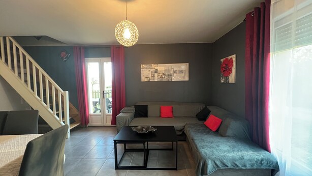 A modern living room with a grey sofa, a coffee table, a staircase, and a dining area.