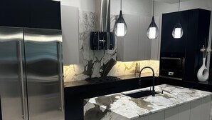 Eine moderne Küche mit einem Edelstahl-Kühlschrank, einer Marmor-Kochinsel, Pendelleuchten und einem eingebauten Ofen.